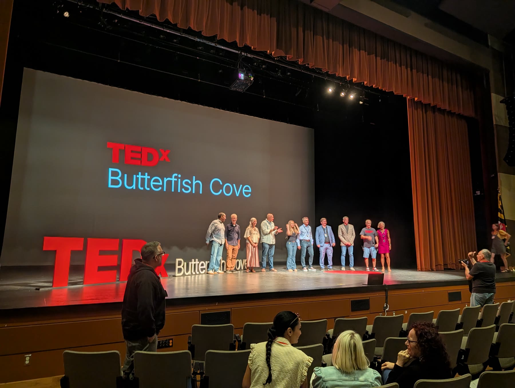 TEDx Butterfish Cove speakers gathered on stage beneath the red TEDx letters at the Ocean City Performing Arts Center