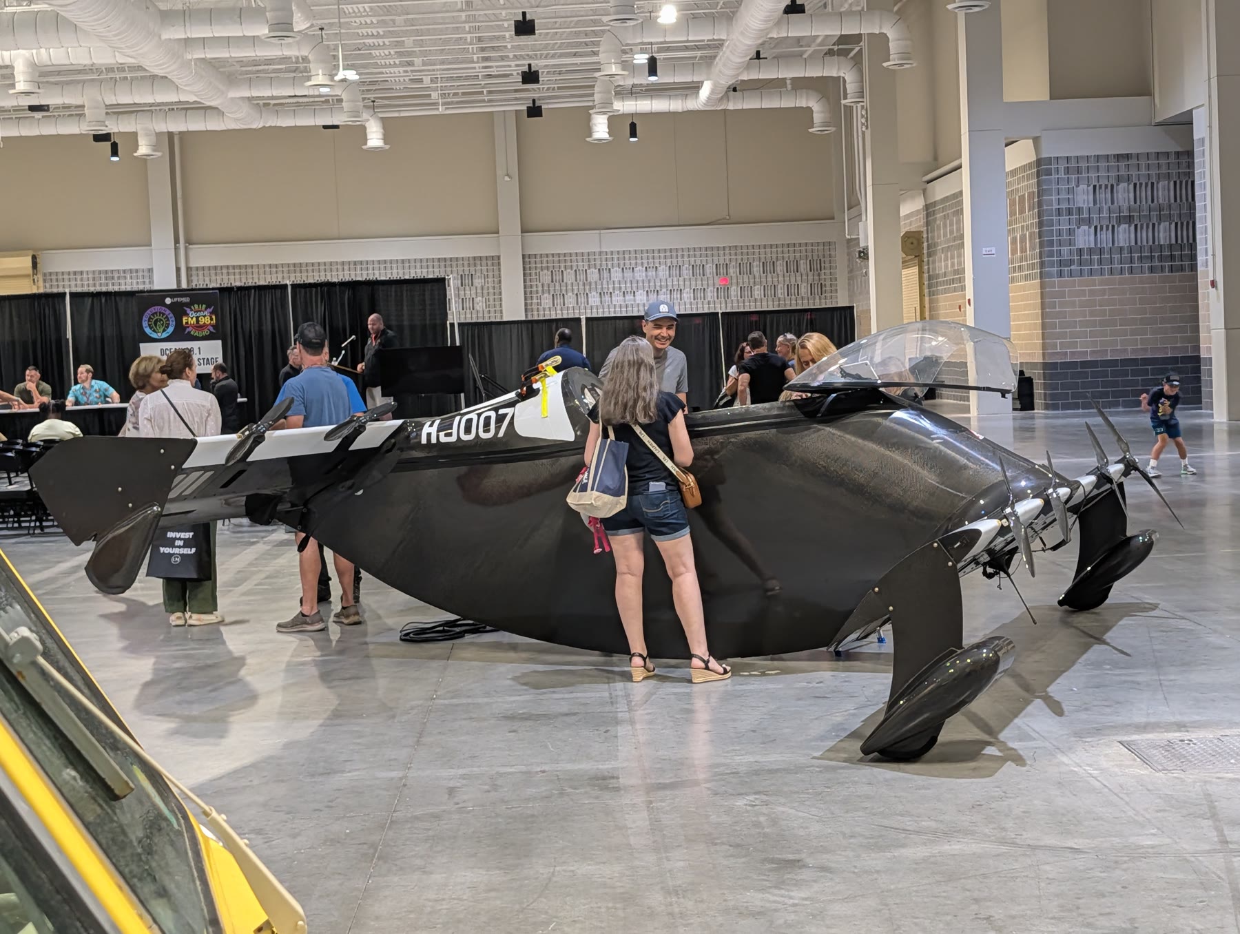 Visitors looking at the black Pivotal BlackFly personal aircraft on the E-Volution Expo floor