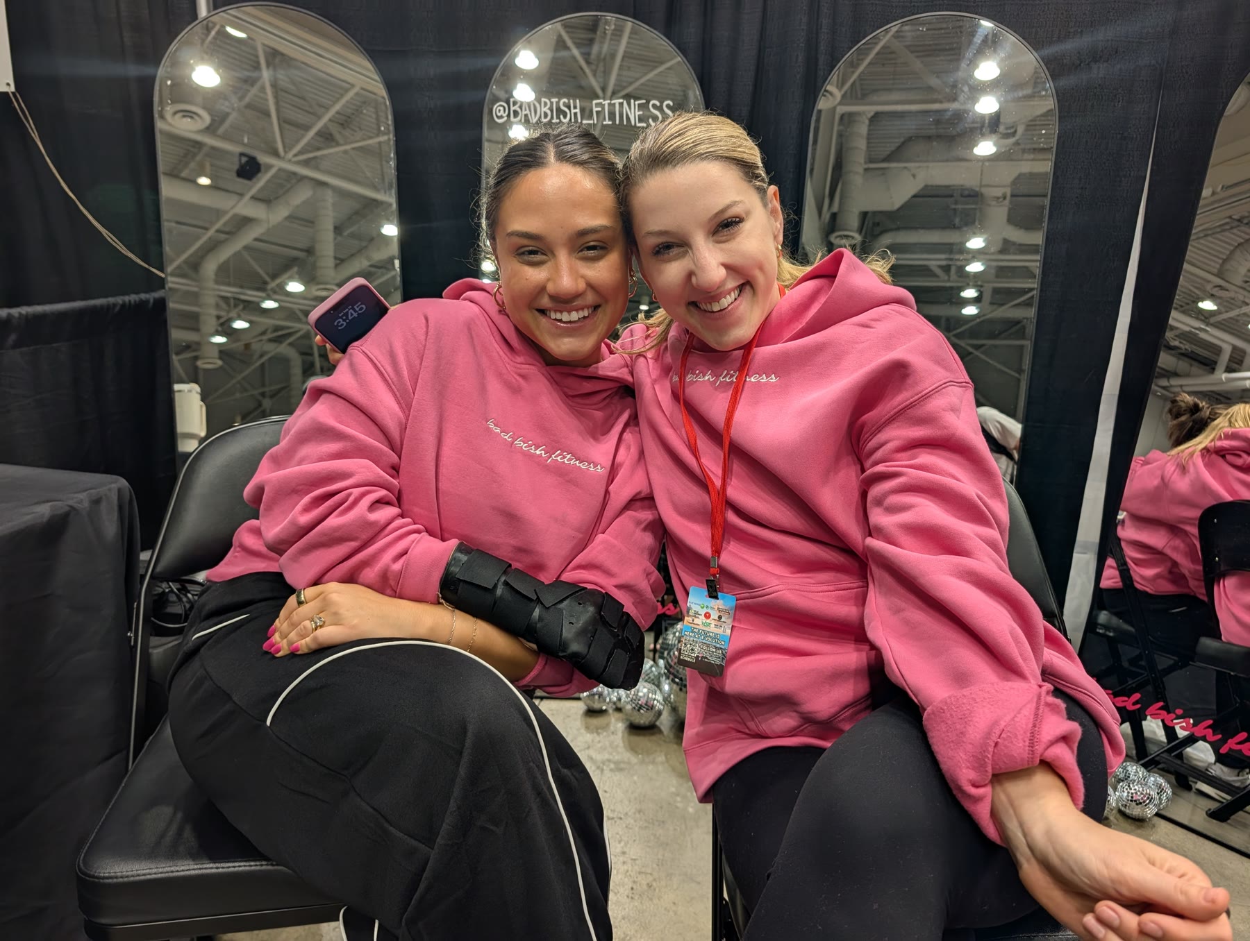 Two women in pink Bad Bish Fitness hoodies at their booth