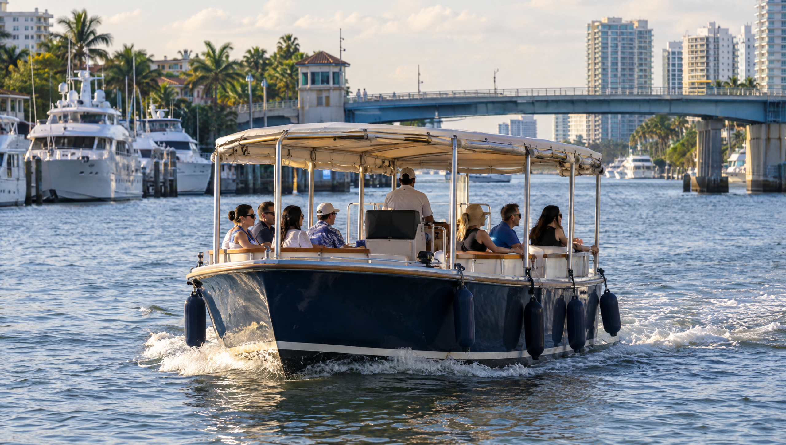 A canopied passenger water taxi crossing the Intracoastal Waterway past moored yachts with a bridge behind