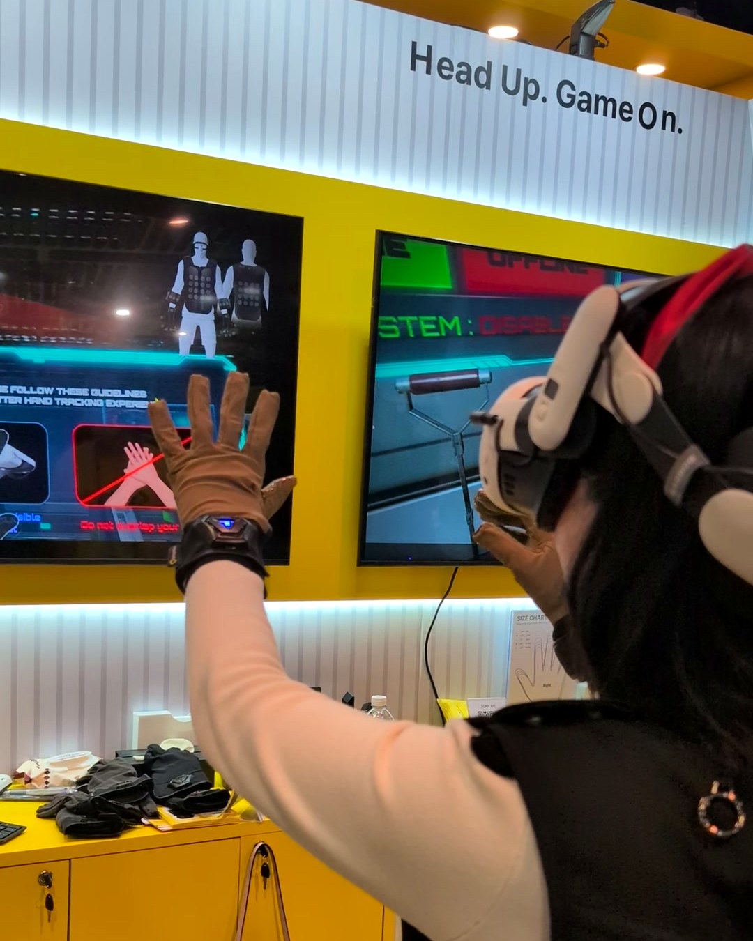 Visitor raising gloved hands under the 'Head Up. Game On.' sign at the bHaptics booth, CES 2025