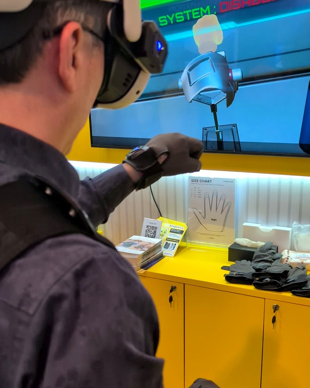 Visitor wearing bHaptics gloves grabbing a virtual object shown on a screen at CES 2025