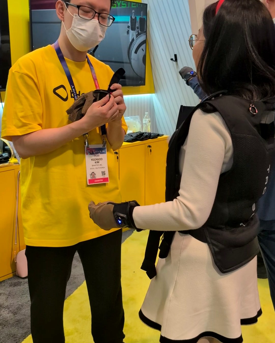 bHaptics staff member fitting a haptic glove on a visitor wearing a TactSuit vest at CES 2025