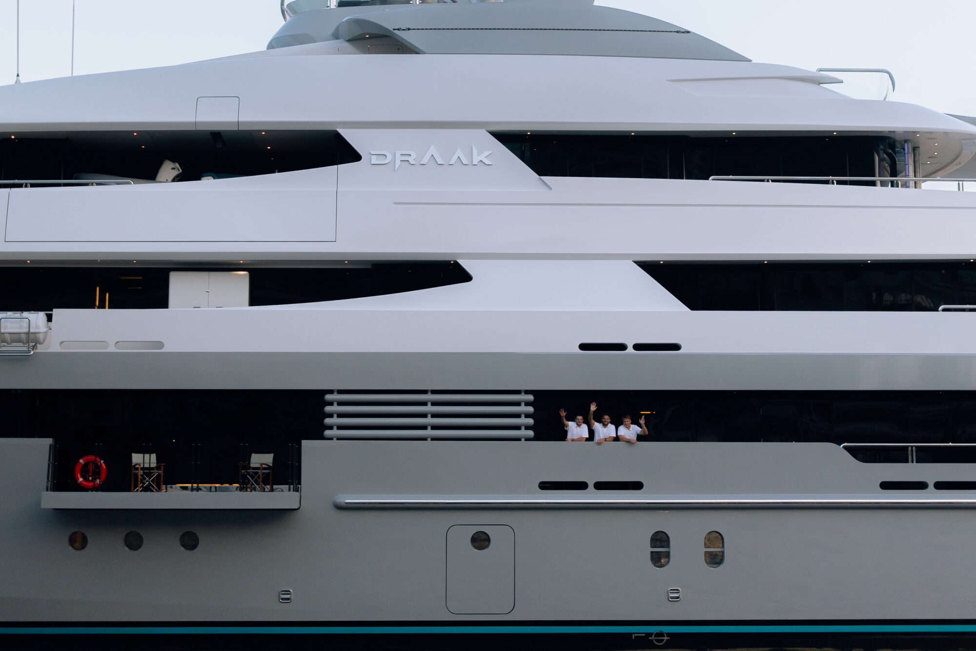 Close-up of Draak's grey superstructure with her name on the side and crew waving from the deck