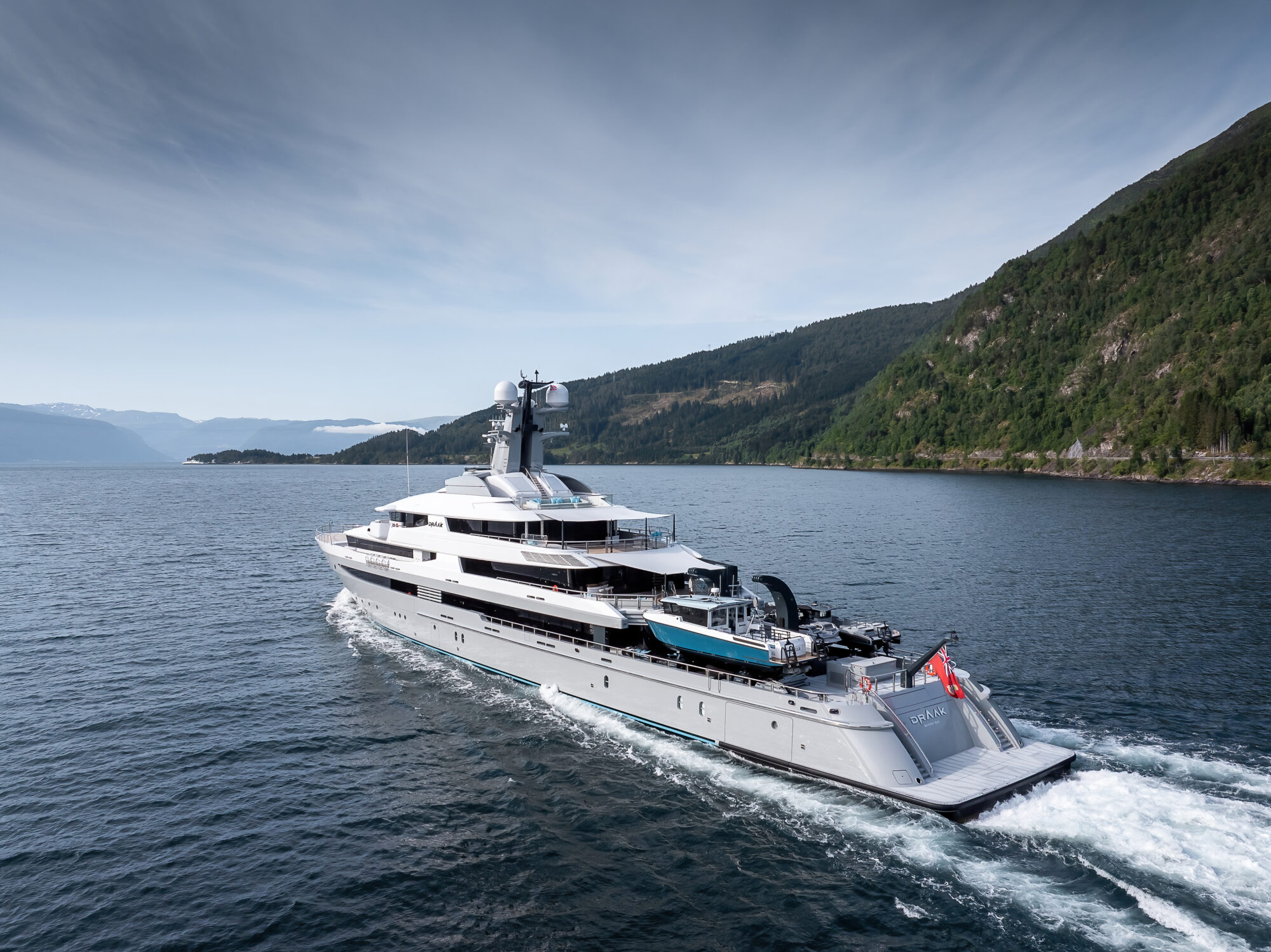 Aerial view of Draak cruising through a fjord, with her dive tenders and crane on the aft deck