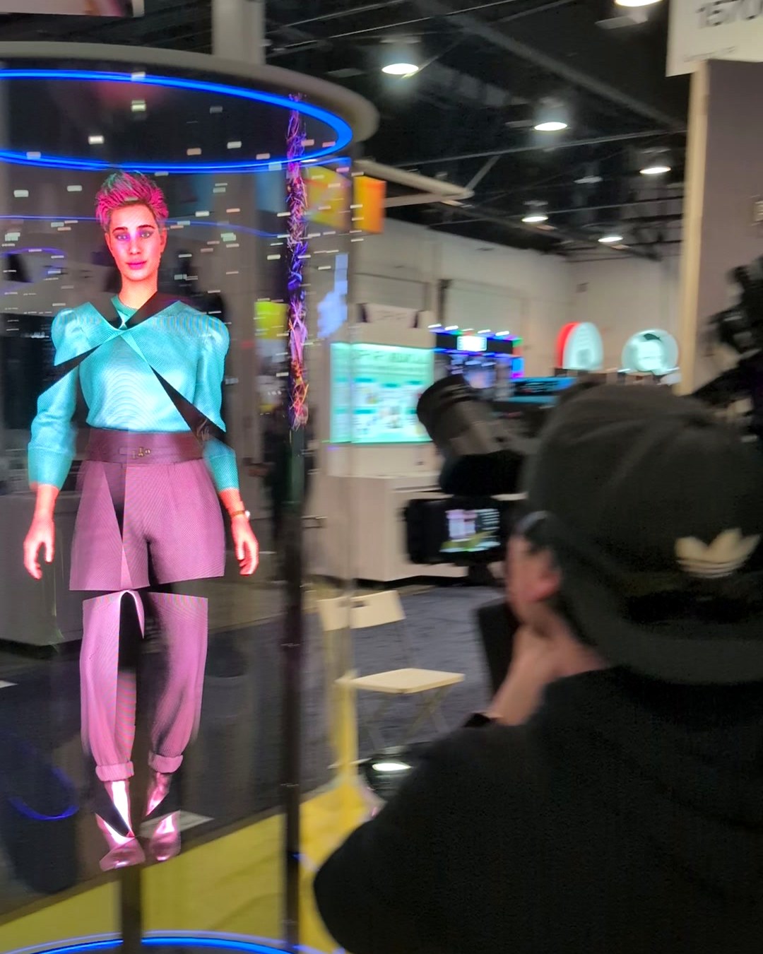 Life-size holographic avatar inside a glass capsule at the HYPERVSN booth, CES 2025, with a camera operator filming