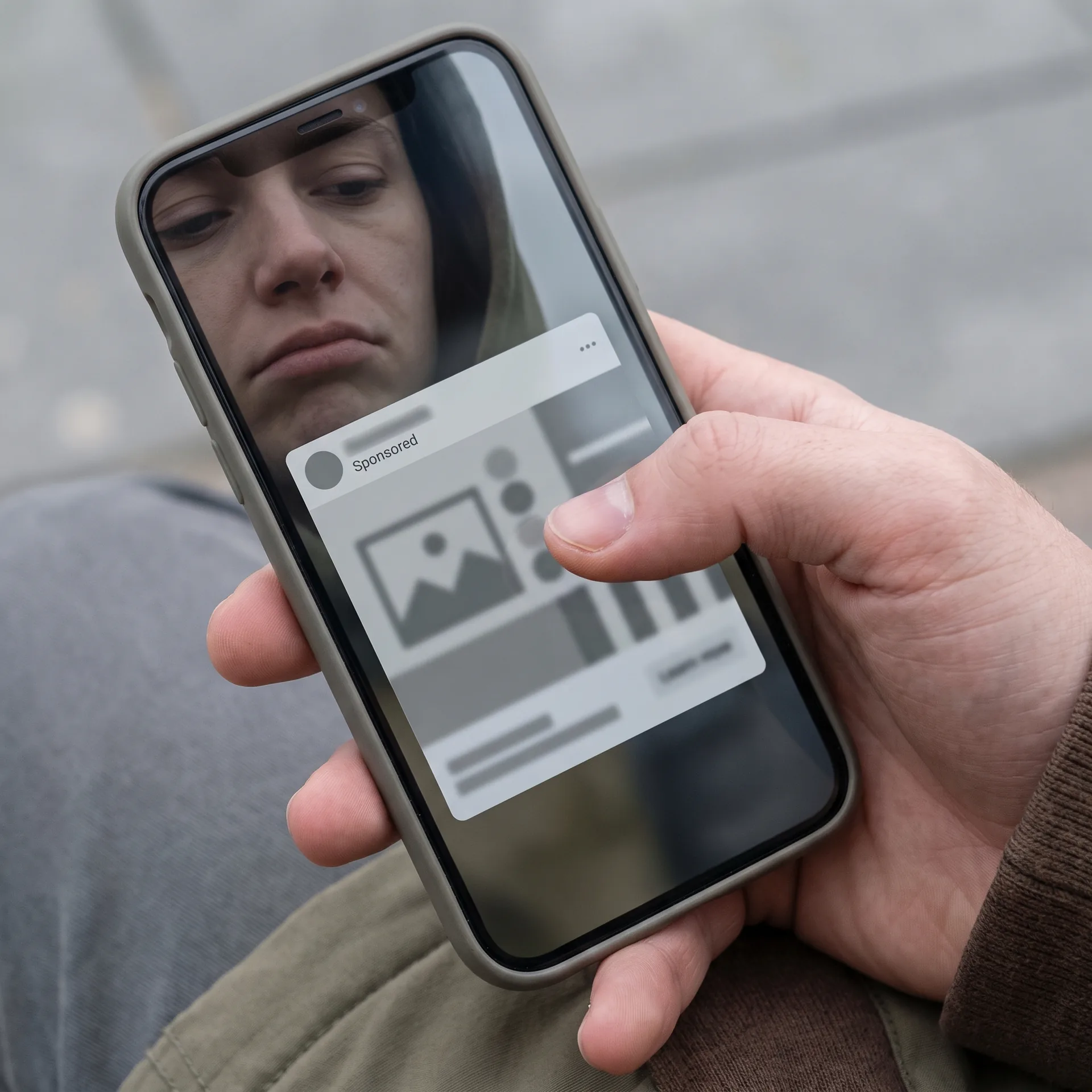 Hand scrolling past a generic paid advertisement on a phone with a bored, indifferent expression